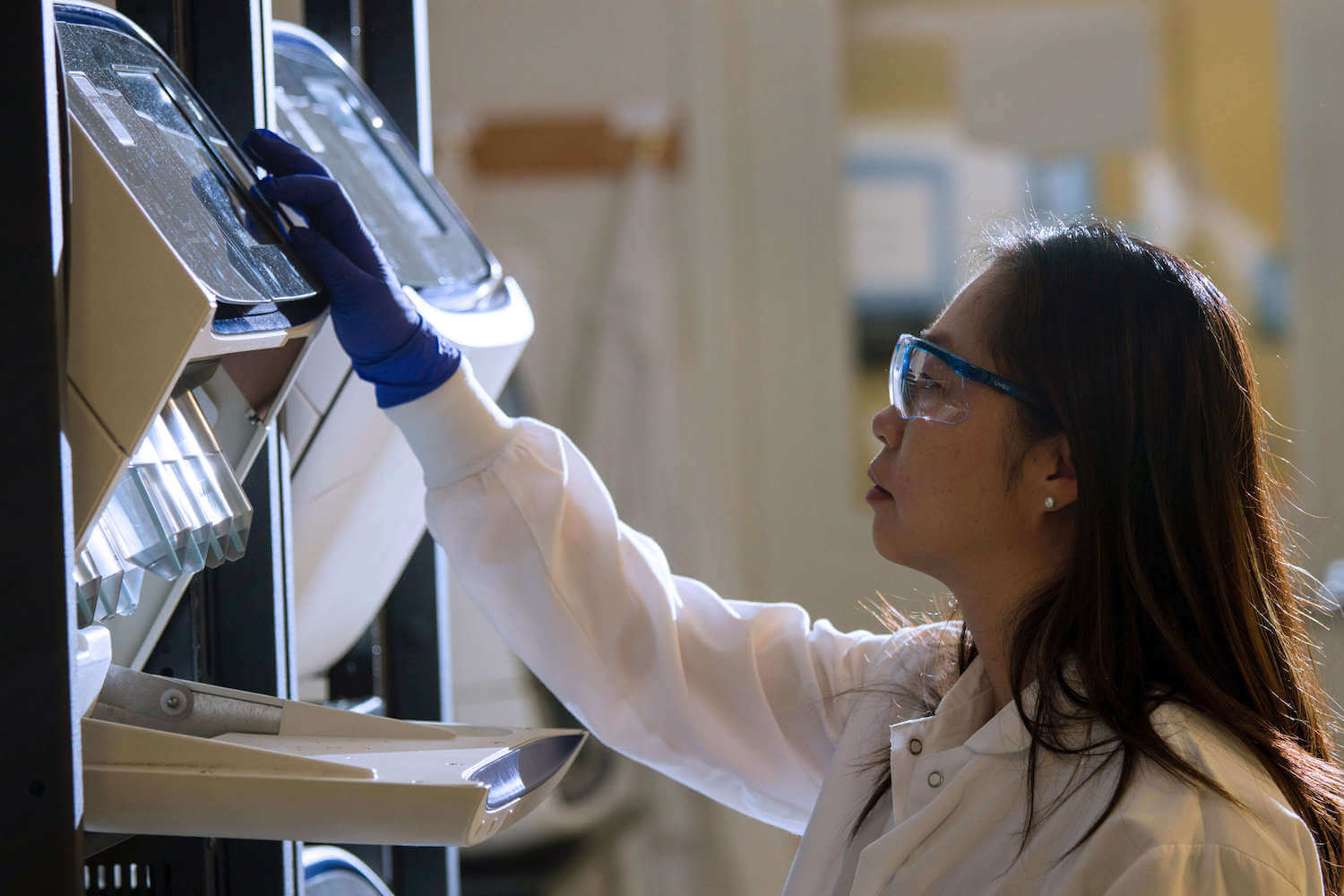 A researcher wearing lab gear and examining a piece of equipment