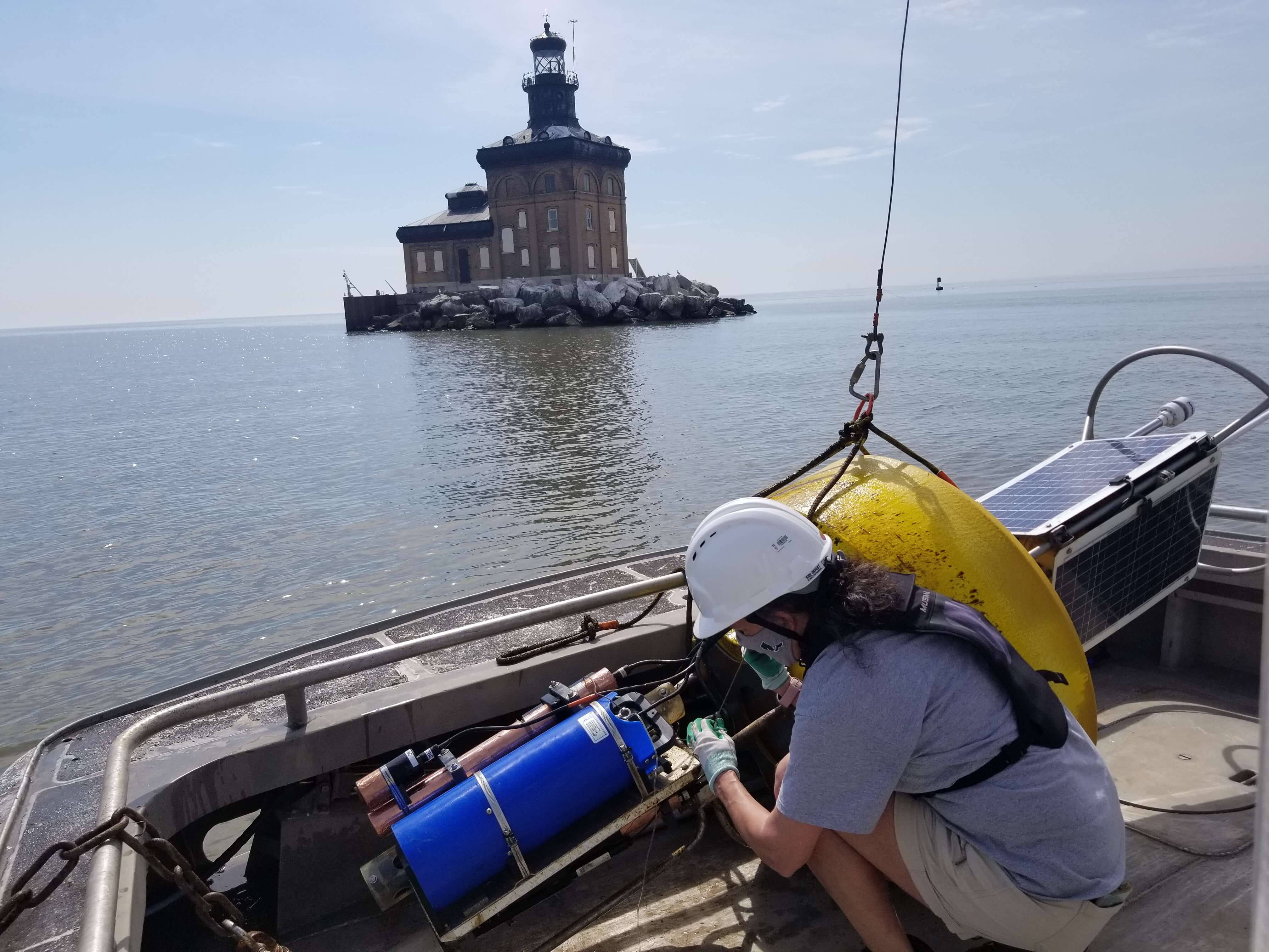 A researcher on a boat with a hard hat with a lighthouse in the distance