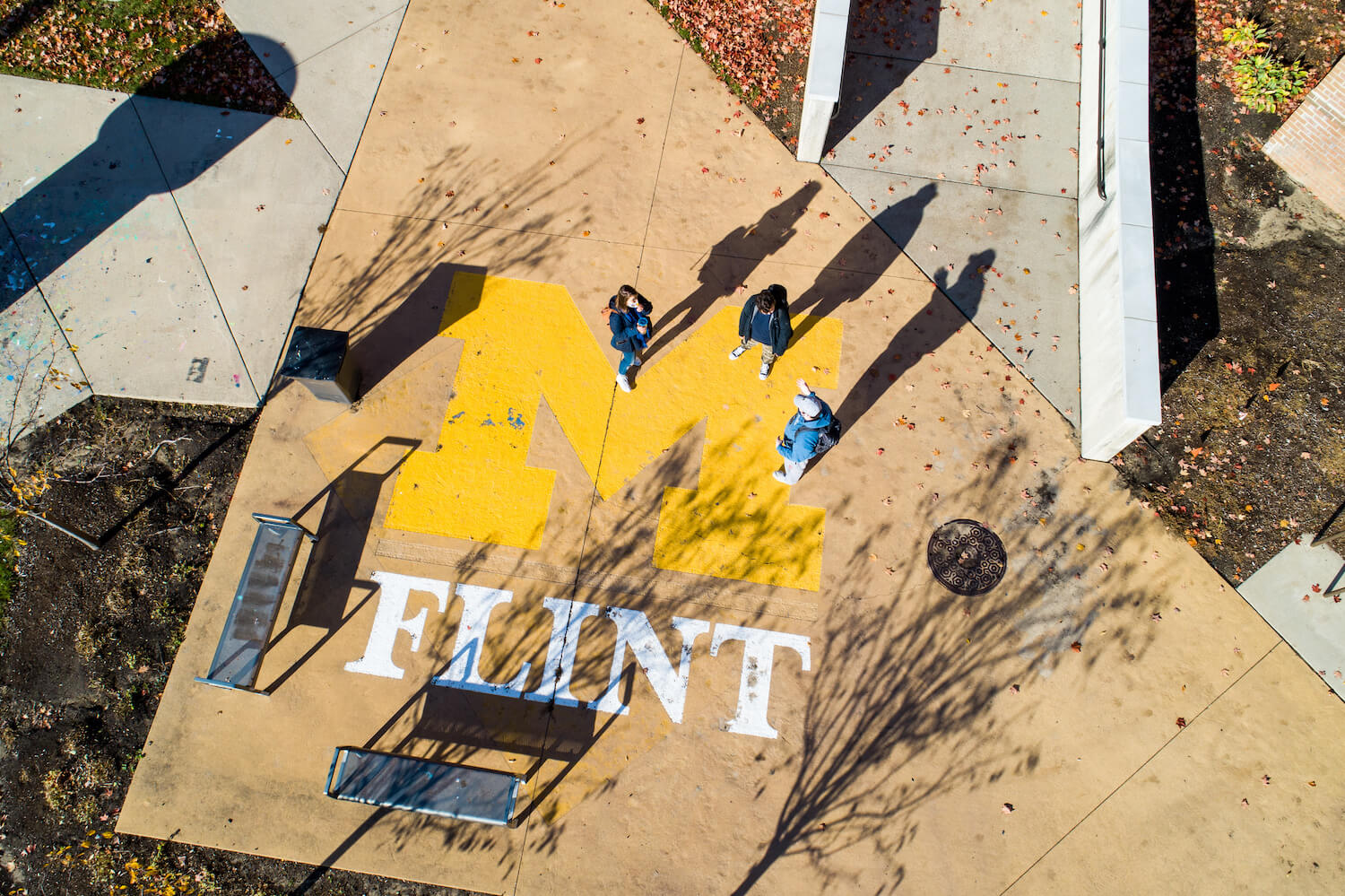 An overhead view of part the University of Michigan-Flint campus in downtown Flint, MI. People are walking over a large block M on the sidewalk with "Flint" written underneath it.