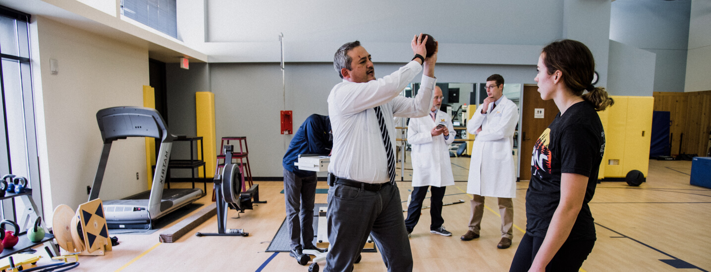 Researchers in lab coats stand around a man holding a ball up in the air